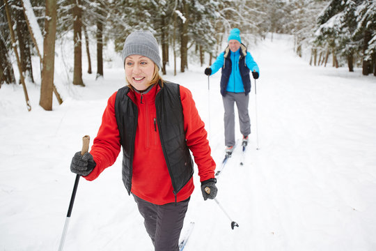 Happy Mature Woman In Sportswear Skiing With Her Husband In Winter Forest