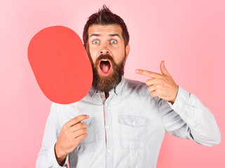 Surprised bearded man hold red name plate. Feeling&emotions. Fashion, beauty, hairdressing, barber salon. Man with beard and mustache shows finger on empty name plate. Blank paper nameplate. Signboard