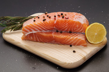 Close up, still life. Ingredients. Fresh orange salmon steak surrounded by lemon, spices and herbs on a wooden board. Black background.