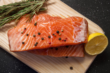 Close up. Ingredients, european cuisine. Fresh salmon steak surrounded by lemon, spices and herbs on a wooden board. Black background.