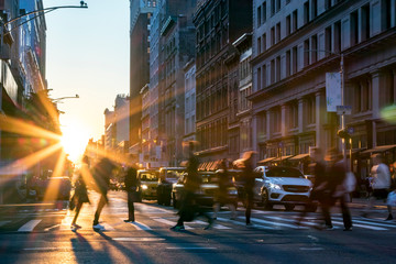Rays of sunlight shine on the busy people walking across an intersection in Midtown Manhattan in New York City