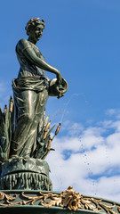Fototapeta na wymiar Female bronze statue with cloudy blue sky background, public gardens, autumn sunshine.