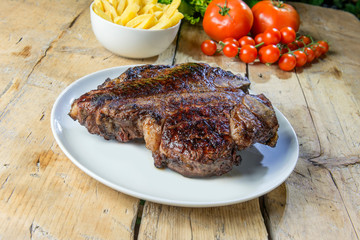 Round dish with grilled porterhouse beef steak on wooden table