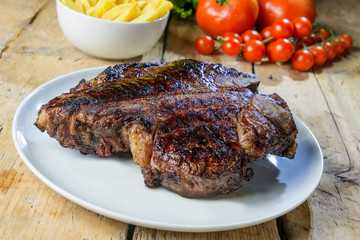 Round dish with grilled porterhouse beef steak on wooden table