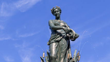 Female bronze statue with cloudy blue sky background, public gardens, autumn sunshine.