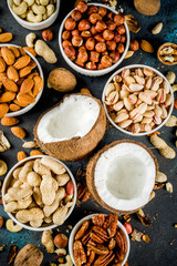 Various types of nuts - walnuts, pecans, peanuts, hazelnuts, coconut, almonds, cashews, in bowls, on a dark blue concrete table top view
