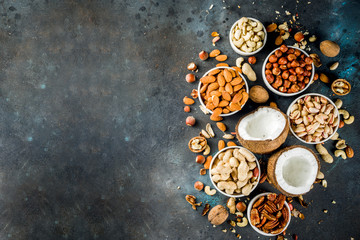 Various types of nuts - walnuts, pecans, peanuts, hazelnuts, coconut, almonds, cashews, in bowls, on a dark blue concrete table top view