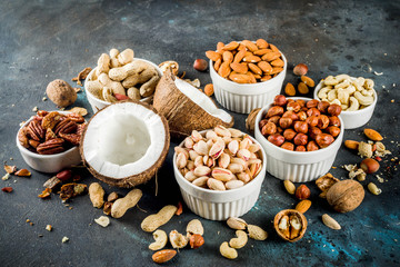 Various types of nuts - walnuts, pecans, peanuts, hazelnuts, coconut, almonds, cashews, in bowls, on a dark blue concrete table top view