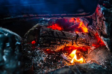 Smoldered logs burned in vivid fire. Atmospheric background with orange flame of campfire. Unimaginable detailed image of bonfire from inside with copy space. Smoke and ashes close up.