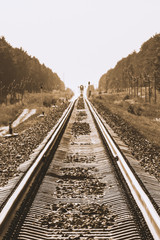 Fototapeta premium Mystic train travels by rail along forest in sepia tones. Railway traffic light and locomotive on railroad in distance. Mirage on railway track. Atmospheric landscape in monochrome.