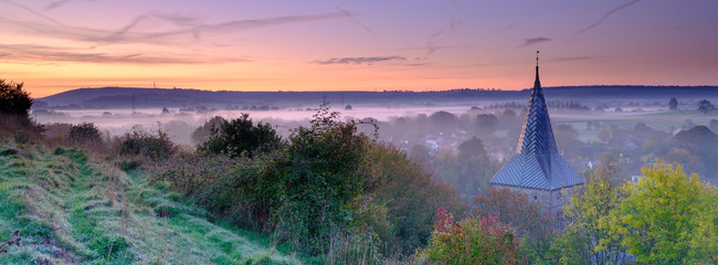 Early morning autumnal mist over East Meon village with Butser Hill and the South Downs in the...
