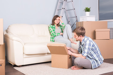 Fototapeta na wymiar Moving, new apartment and relocation concept - Young man helping his wife with unpacking