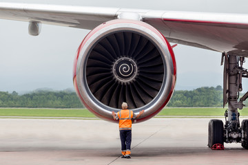 Engineer checks turbine engine of modern passenger airplane on runway. Service and maintenance of airplanes. Aviation and transportation.