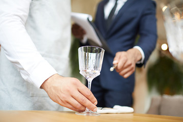 Close-up of waiter puts a wineglass on the table under the supervision of the restaurant manager