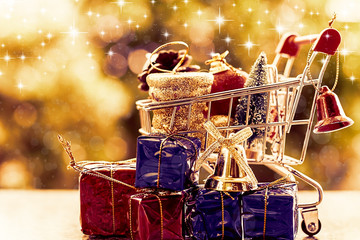 Full of Xmas decorative items in mini shopping cart or trolley against blurred natural green background for Christmas and New Year festival concept (added glowing star and color filter effect)