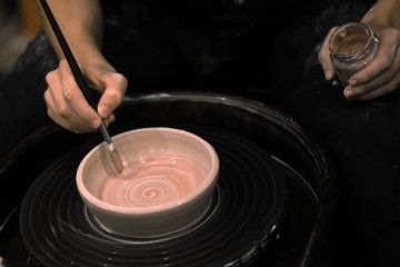 A hand with a brush paints a clay product on a potter's wheel