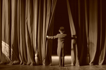 Actor in a tuxedo and hat looks behind the theater curtain