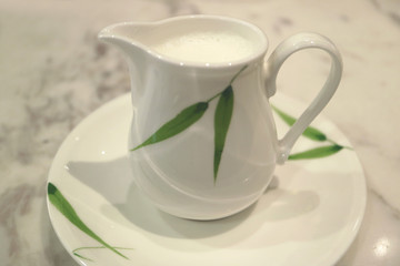 Closed up white with green pattern ceramic milk pitcher on white marble table 