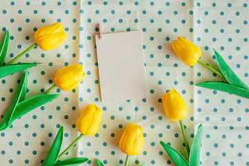 Artificial yellow tulips with white paper card on blue polka dot fabric or tablecloth for nature and springtime concept
