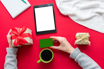 Female hands, woman holding a Business card and gift. Cup of coffee or tea, tablet pc, red table, gifts boxes for the holidays, background with copy space for advertisement, top view