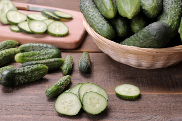 Fresh green cucumbers in a basket and slices of cucumbers on a brown wooden table. vegetables