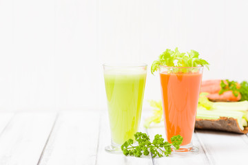 Carrot and celery juice with fresh vegetables on bark plates on wooden background.