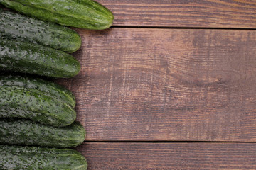 Fresh green framed cucumbers on a brown wooden table with space for an inscription