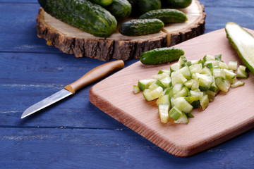 Lots of chopped cucumber slices on a cutting board with a knife on a blue wooden table