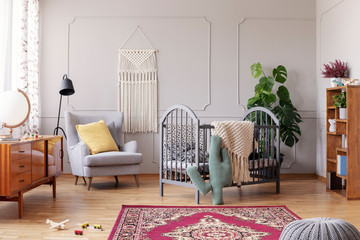Cozy baby room with comfortable armchair with yellow pillow and grey wooden crib, real photo