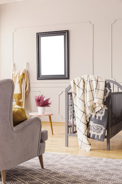 Mockup on the wall of mid century baby room with grey armchair, crib with blankets and heather in white pot on the table