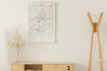 Map in white frame, flower in a glass vase on wooden shelf, next to wooden hanger, real photo with...
