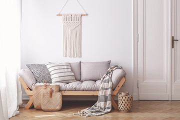 Handmade wicker bags on herringbone parquet floor of a warm living room interior with an artisan, beige macrame on a white wall - obrazy, fototapety, plakaty