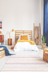 Yellow pillow and blanket on comfortable white wooden bed in teenager bedroom with stripped carpet on the floor