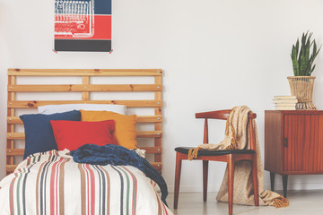 Blue, red and orange pillows on single bed with stripped duvet and wooden headboard in oldschool...