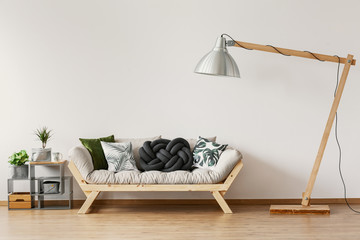 Oversize industrial lamp above scandinavian settee with pillows in stylish living room, real photo with copy space