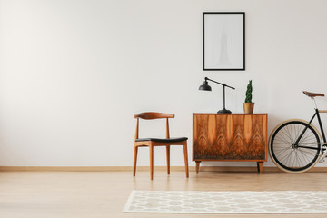 Stylish chair next to retro cabinet and vintage bike in scandinavian minimal interior, real photo...