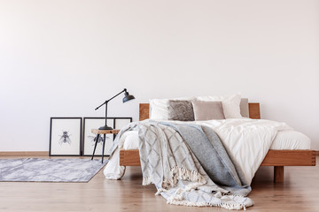 Comfortable king size bed with pillows and blankets in bright bedroom interior with rustic carpet on the floor, real photo with copy space - obrazy, fototapety, plakaty