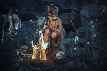 Caveman, manly boy at the fire. Scary young primitive boy outdoors near bonfire. Witch craft concept. Angry caveman, manly boy with horns near bonfire. Prehistoric tribal man outdoors on nature