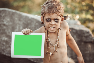 Caveman, manly boy holding tablet PC with green screen. Funny young primitive boy outdoors....