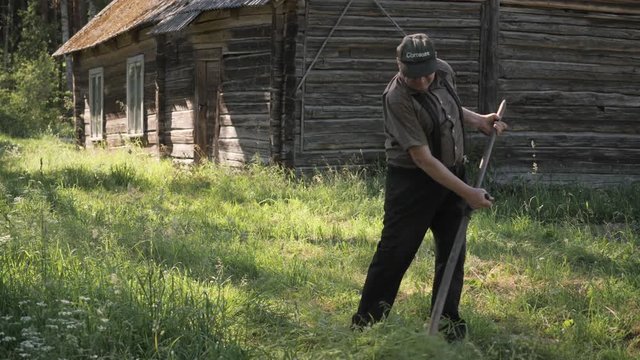 old man cutting grass with scythe