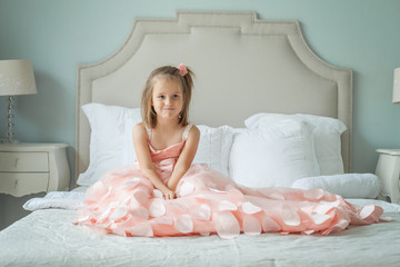 Funny little girl in pink dress sitting on bed