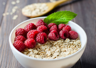 Healthy vegetarian food. Oatmeal with raspberry. Wooden spoon with cereals. Brown wooden background.