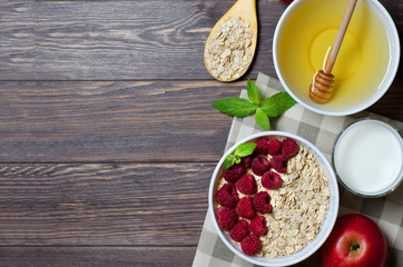 Healthy vegetarian food. Oatmeal with raspberry. Wooden spoon with cereals, milk in a glass, apple. Brown wooden background. Flat Lay. Copy space