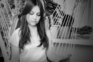 Beautiful girl with long dark hair reads a book sitting in a hammock on the balcony, BW