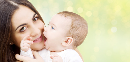 family and motherhood concept - happy smiling young mother and little baby over green background with festive lights