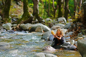 little girl bathes a doll in a mountain river