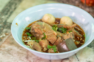Instant noodles in soup with pork, meatballs and chicken broth in bowl at the restaurant. Thai street food. Soft focus and blur. 