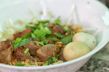 Instant noodles with pork broth, meatballs and garlics and herbs in bowl at the restaurant. Thai street food. Soft focus and blur. 