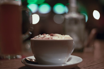 Blurred background conveying the atmosphere of an evening restaurant, a cup of cappuccino on the table close-up