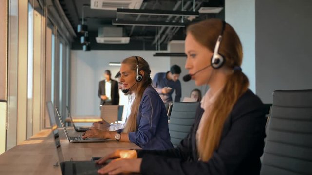 Female operator agent with headsets working in a call centre. They speaking about transaction and purchasing corporate plan of their big company. 4K UltraHD refocusing between people.